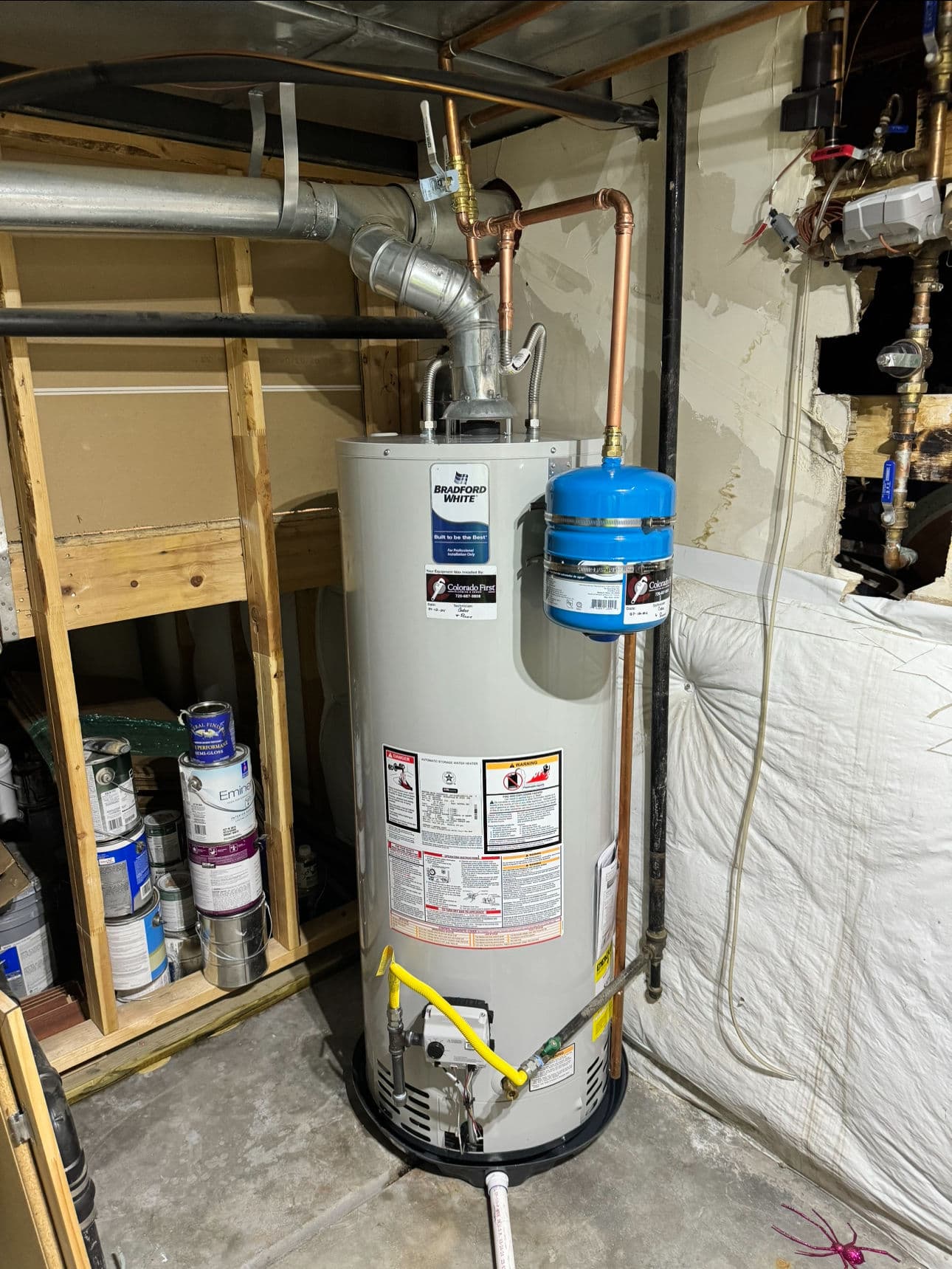 Water heater installation in basement with copper pipes and safety features.