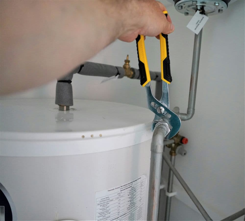 Person using adjustable pliers to repair a hot water heater pipe.