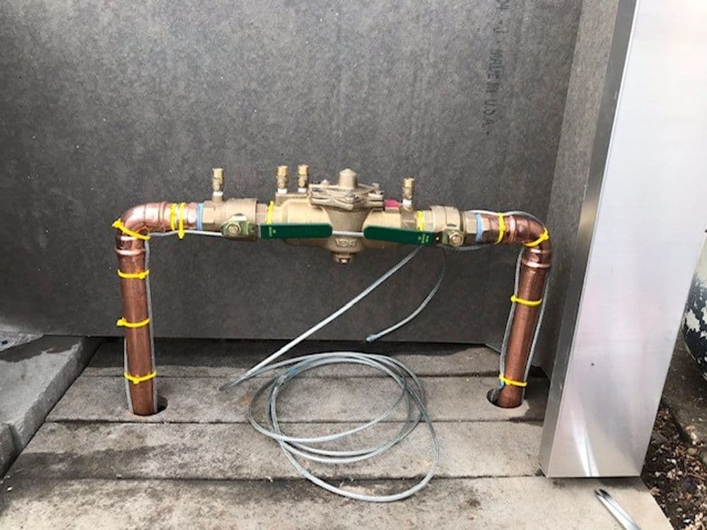 Water meter installation with copper pipes and valve, secured with yellow ties and wires.